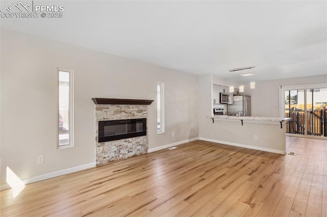 unfurnished living room with light hardwood / wood-style flooring and a stone fireplace