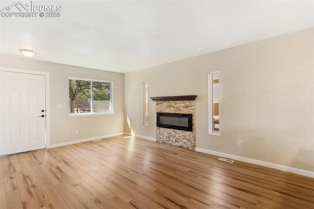 unfurnished living room featuring light hardwood / wood-style floors and a stone fireplace