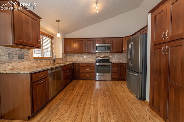 kitchen with appliances with stainless steel finishes, light wood-type flooring, hanging light fixtures, and lofted ceiling