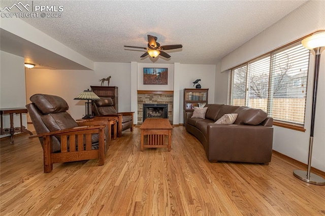 living room with ceiling fan, a fireplace, light hardwood / wood-style floors, and a textured ceiling