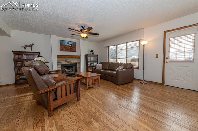 living room with a fireplace, a textured ceiling, light hardwood / wood-style flooring, and ceiling fan