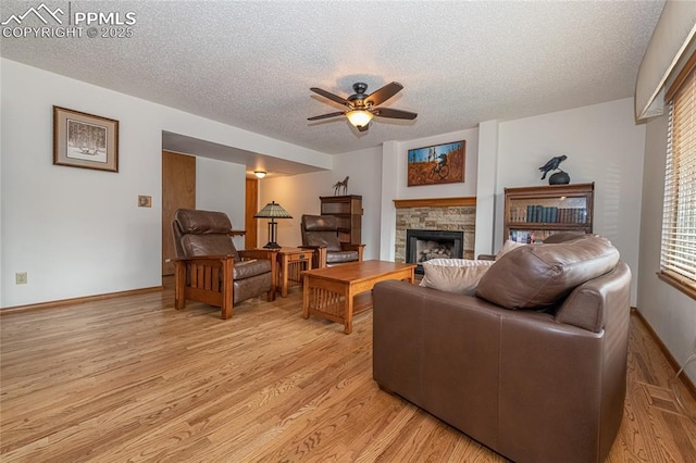 living room featuring a fireplace, ceiling fan, a textured ceiling, and light hardwood / wood-style flooring