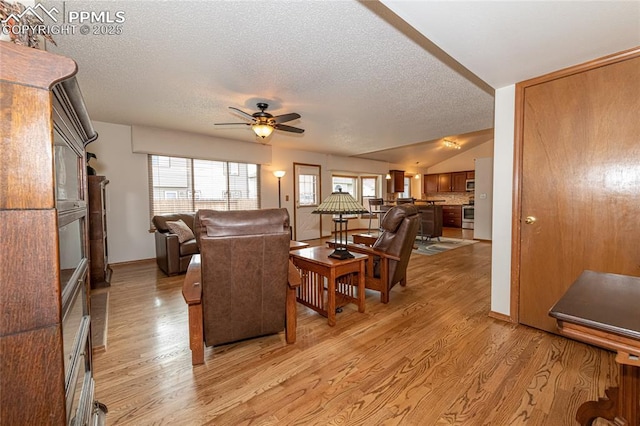 living room with lofted ceiling, ceiling fan, a textured ceiling, and light wood-type flooring