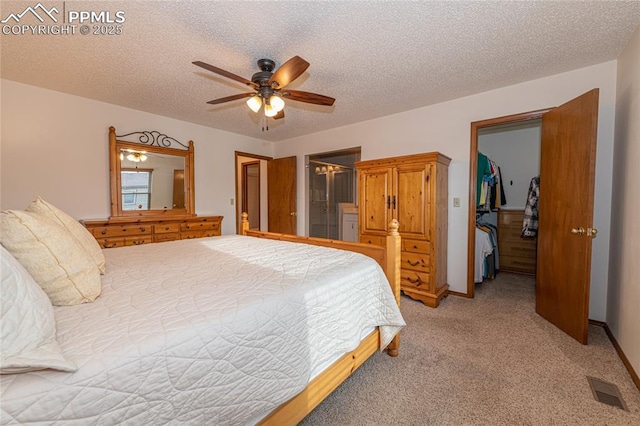 carpeted bedroom with a walk in closet, ceiling fan, a closet, and a textured ceiling