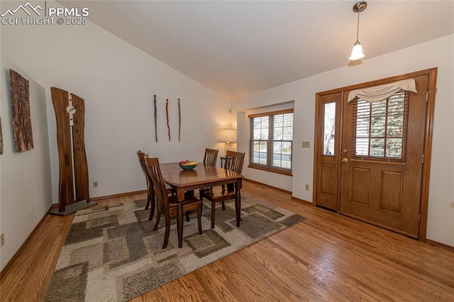 dining room featuring a textured ceiling, light wood-type flooring, and vaulted ceiling