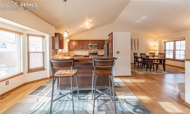 kitchen featuring kitchen peninsula, appliances with stainless steel finishes, backsplash, vaulted ceiling, and sink