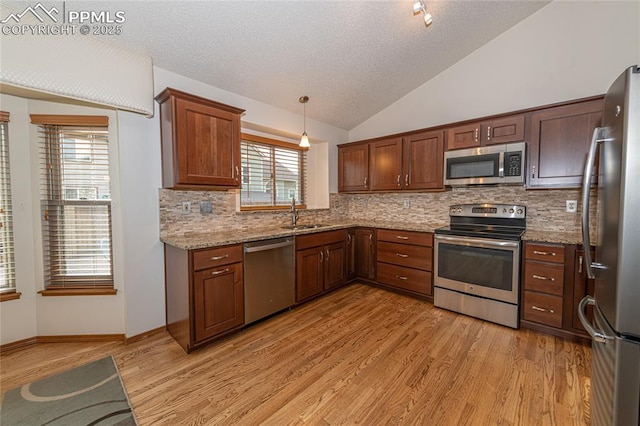 kitchen with pendant lighting, lofted ceiling, light stone countertops, light hardwood / wood-style floors, and stainless steel appliances