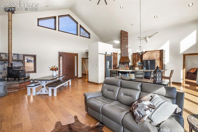 living room with high vaulted ceiling, a barn door, light wood-style flooring, a wood stove, and an inviting chandelier