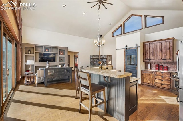 kitchen with decorative light fixtures, backsplash, a barn door, high vaulted ceiling, and hardwood / wood-style floors