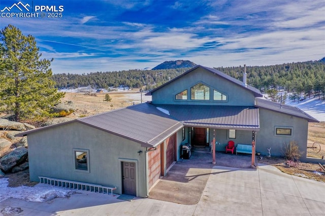 rustic home featuring metal roof, driveway, stucco siding, and a view of trees