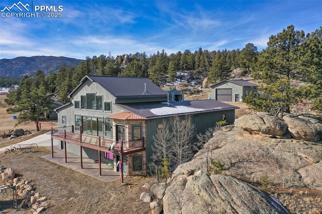 back of property featuring a deck with mountain view, a forest view, a garage, and metal roof