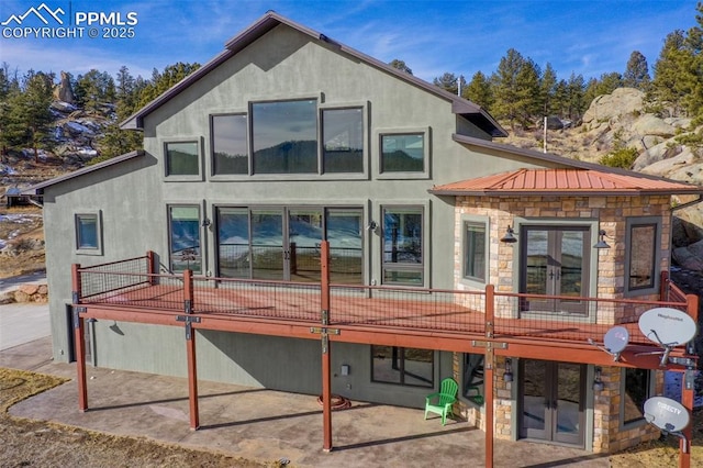 back of house featuring stone siding, french doors, metal roof, and a wooden deck