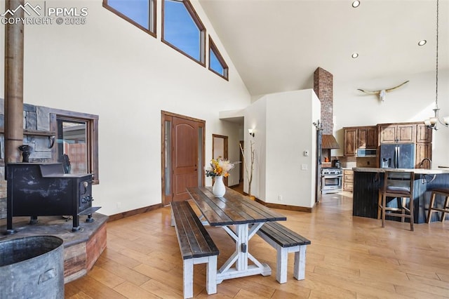 dining room with a high ceiling, baseboards, light wood finished floors, a wood stove, and an inviting chandelier