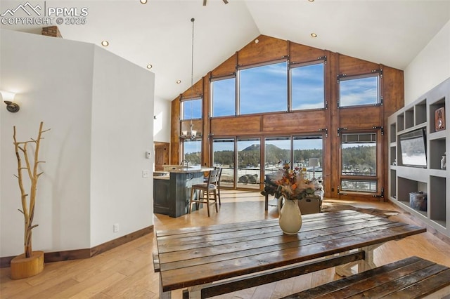 dining space featuring high vaulted ceiling, light wood-style flooring, and baseboards