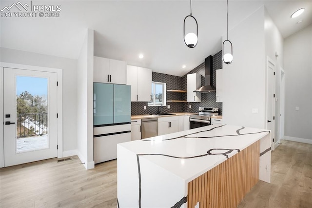 kitchen featuring stainless steel appliances, wall chimney range hood, tasteful backsplash, pendant lighting, and white cabinets