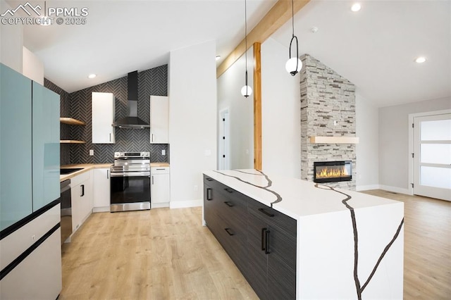 kitchen with stainless steel appliances, wall chimney range hood, decorative light fixtures, a fireplace, and white cabinetry