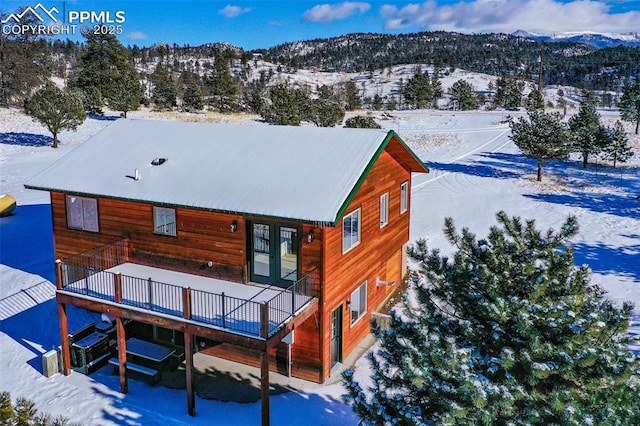 snow covered house featuring a deck with mountain view and french doors