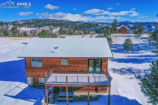 snow covered rear of property with french doors and a deck with mountain view