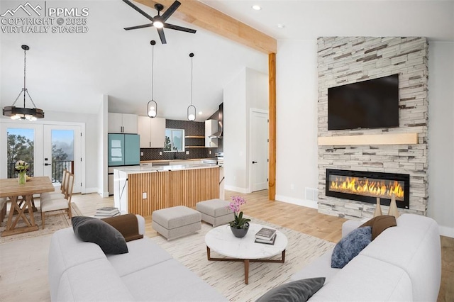 living room featuring french doors, light hardwood / wood-style flooring, lofted ceiling with beams, a fireplace, and ceiling fan with notable chandelier