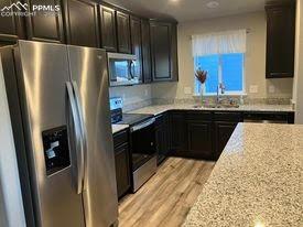 kitchen featuring stainless steel appliances, light hardwood / wood-style floors, sink, light stone counters, and dark brown cabinets