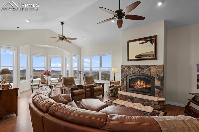 living room with a stone fireplace, ceiling fan, hardwood / wood-style floors, and vaulted ceiling