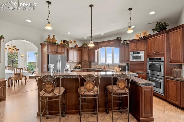 kitchen featuring a wealth of natural light, stainless steel appliances, dark stone counters, a spacious island, and pendant lighting