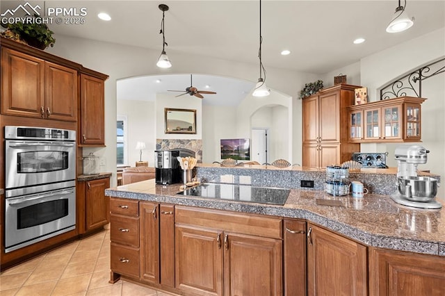 kitchen featuring pendant lighting, a stone fireplace, ceiling fan, black electric cooktop, and double oven