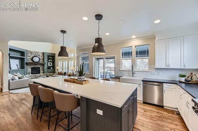 kitchen featuring white cabinetry, dishwasher, sink, a stone fireplace, and pendant lighting