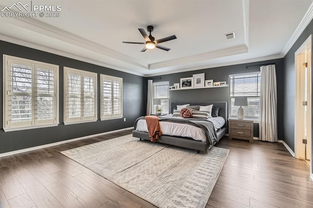 bedroom featuring ceiling fan, ornamental molding, dark wood-type flooring, and a tray ceiling