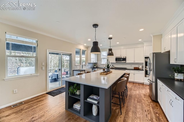 kitchen featuring stainless steel appliances, hardwood / wood-style flooring, white cabinets, a center island, and hanging light fixtures