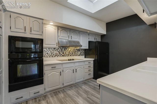 kitchen with gray cabinetry, black appliances, a skylight, decorative backsplash, and light hardwood / wood-style floors