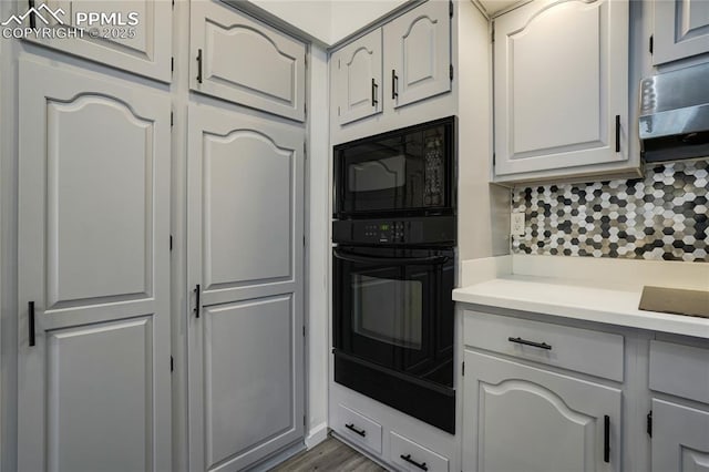 kitchen with black appliances, light wood-type flooring, white cabinetry, and backsplash