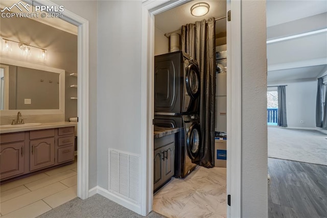 laundry area featuring light tile patterned flooring, stacked washer / dryer, and sink