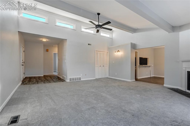 unfurnished living room featuring beamed ceiling, ceiling fan, carpet floors, and a high ceiling