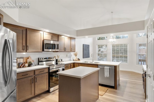 kitchen featuring sink, a center island, stainless steel appliances, backsplash, and light wood-type flooring