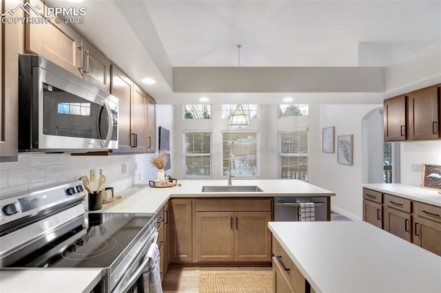 kitchen featuring kitchen peninsula, appliances with stainless steel finishes, backsplash, sink, and light hardwood / wood-style flooring