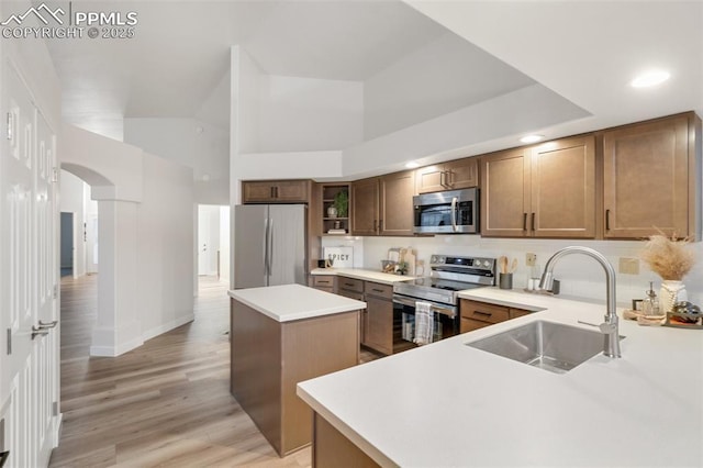 kitchen with a high ceiling, sink, light hardwood / wood-style floors, a kitchen island, and stainless steel appliances