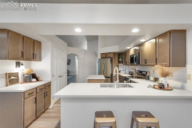 kitchen with sink, stainless steel appliances, kitchen peninsula, a breakfast bar area, and light wood-type flooring