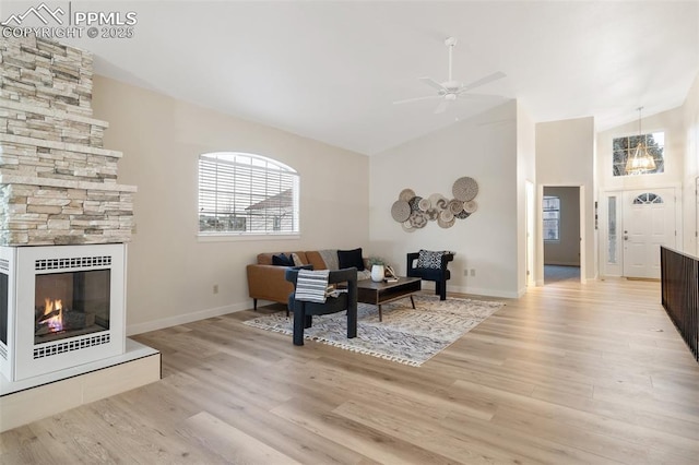 living room with ceiling fan, a large fireplace, vaulted ceiling, and light wood-type flooring