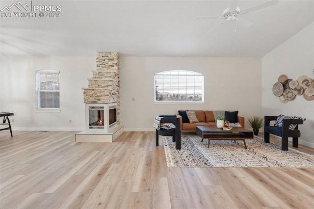 living room with ceiling fan, a stone fireplace, and light hardwood / wood-style flooring