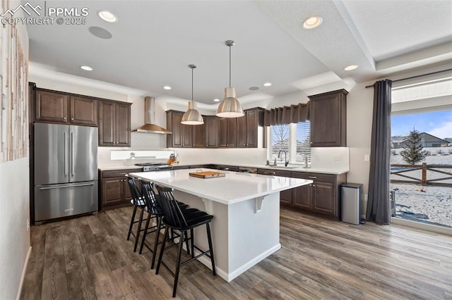 kitchen featuring high quality fridge, hanging light fixtures, a kitchen island, wall chimney exhaust hood, and sink