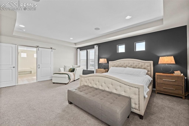 carpeted bedroom featuring a raised ceiling, a barn door, and ensuite bath