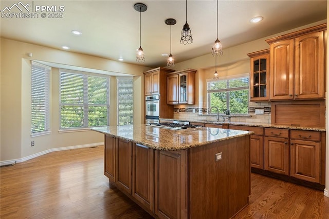 kitchen featuring decorative backsplash, light stone counters, sink, pendant lighting, and a center island