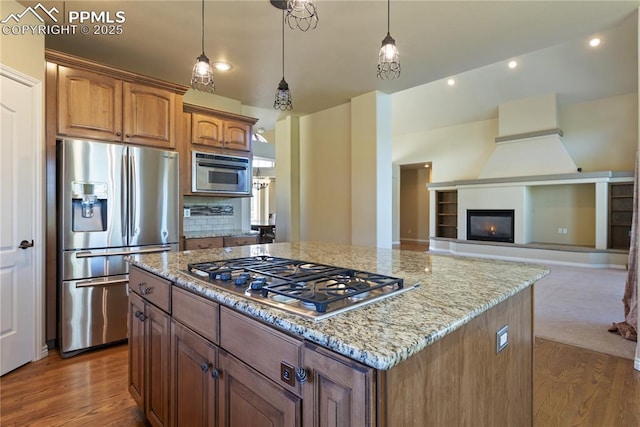 kitchen with stainless steel appliances, tasteful backsplash, light stone counters, pendant lighting, and a kitchen island