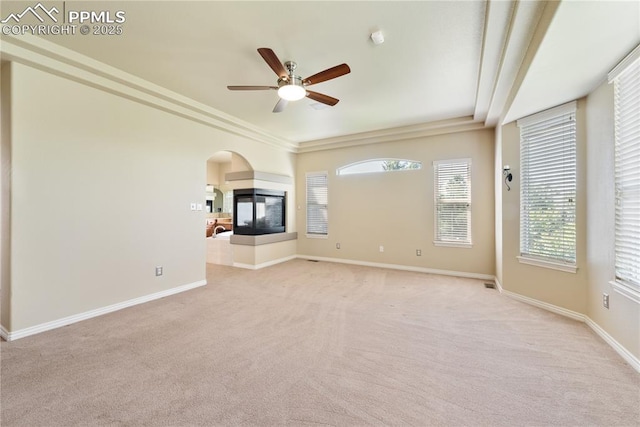 unfurnished living room with a multi sided fireplace, ceiling fan, crown molding, and light colored carpet