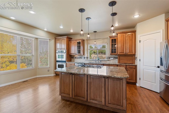 kitchen featuring a center island, backsplash, hanging light fixtures, stone countertops, and stainless steel appliances