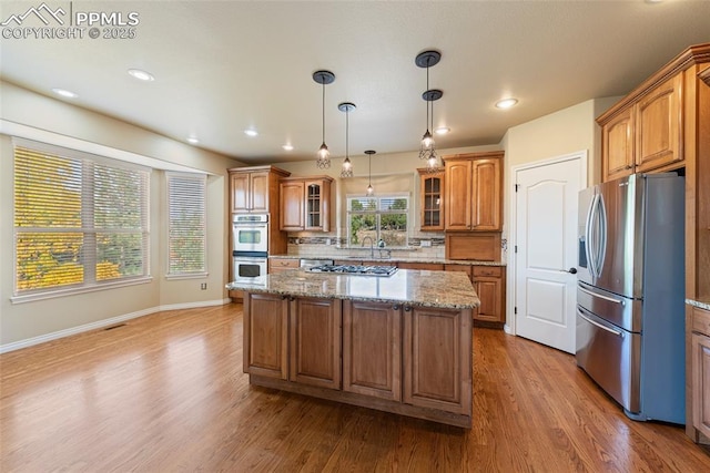 kitchen with backsplash, stainless steel appliances, stone counters, hardwood / wood-style floors, and a kitchen island