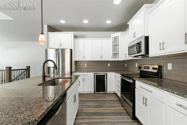 kitchen featuring stainless steel appliances, sink, dark stone countertops, wine cooler, and hanging light fixtures