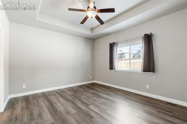 empty room featuring a tray ceiling, ceiling fan, and wood-type flooring