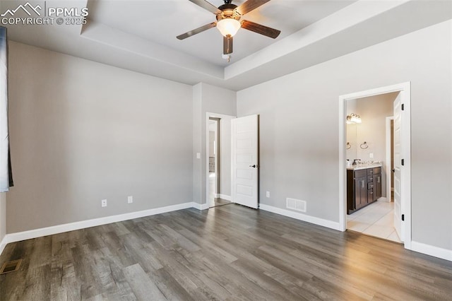 unfurnished bedroom featuring ensuite bathroom, ceiling fan, a raised ceiling, and light hardwood / wood-style flooring